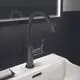 Waschtischarmatur in Magnetic Grey von Ideal Standard, mit hohem Auslauf und Bedienteil, installiert auf einem weißen Becken, vor schwarzer Fliesenwand.